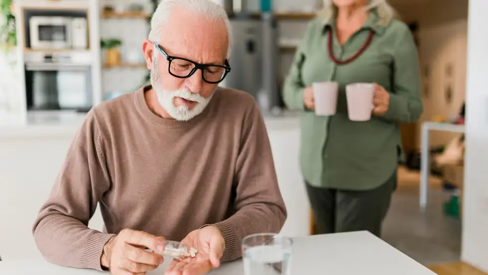 senior-man-sitting-at-home-taking-medication-pills